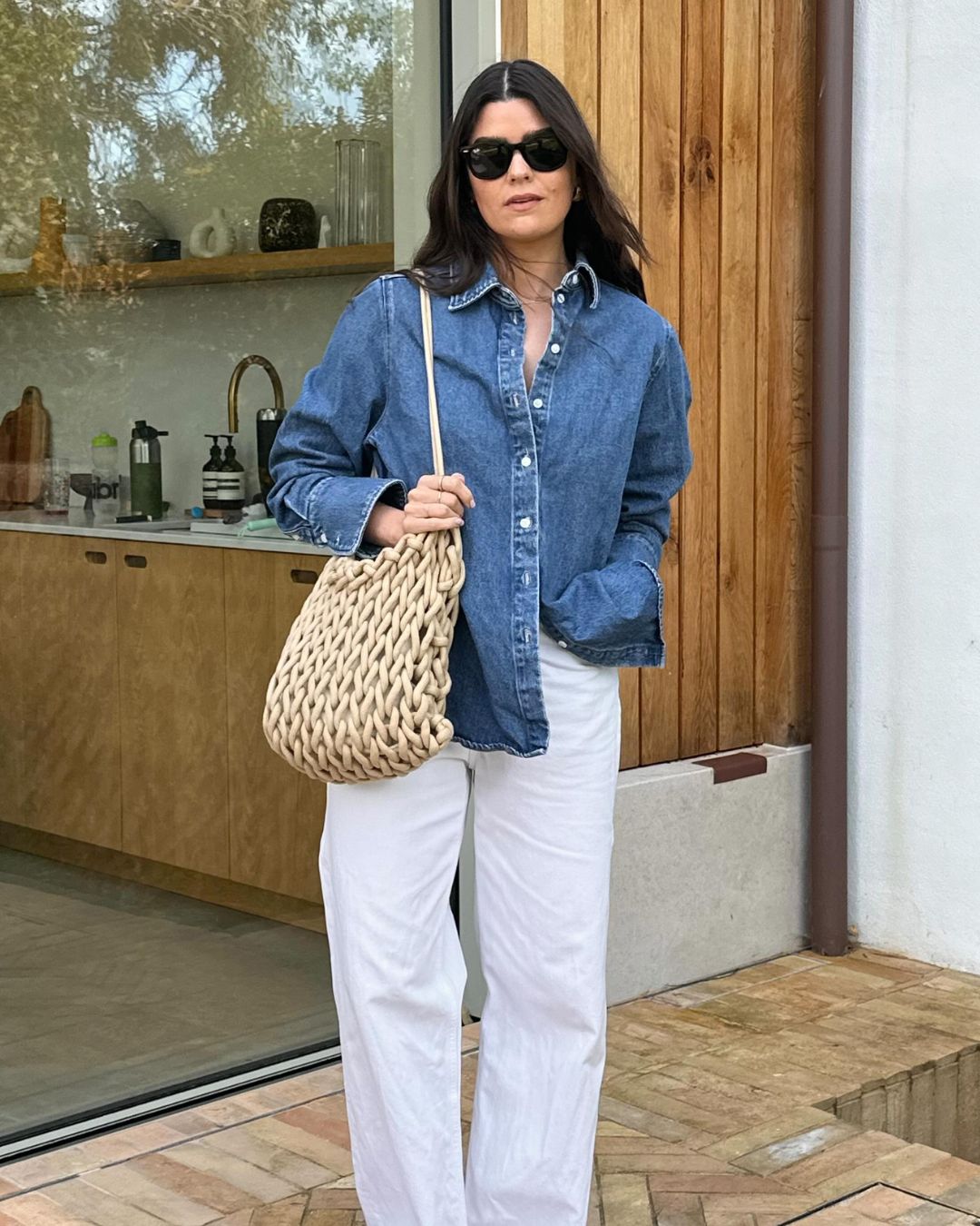 Influencer @theannaedit wears a denim shirt with white jeans and a woven bag.