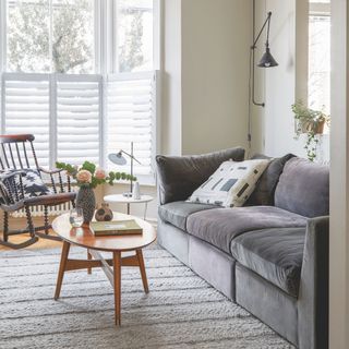 Neutral living room with a grey sofa and a wooden coffee table in front. Towards the window is a wooden rocking chair