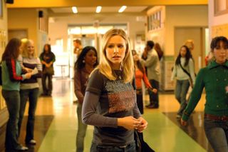 kristen bell wearing a tshirt over long sleeves standing in a high school hallway in the tv show veronica mars