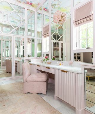 pink dressing area with fluted dressing table, floral wallpapered ceiling and glass fronted cabinets