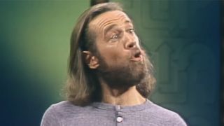 George Carlin, long brown hair and grey shirt, performing standup, footage used in HBO's doc George Carlin's American Dream