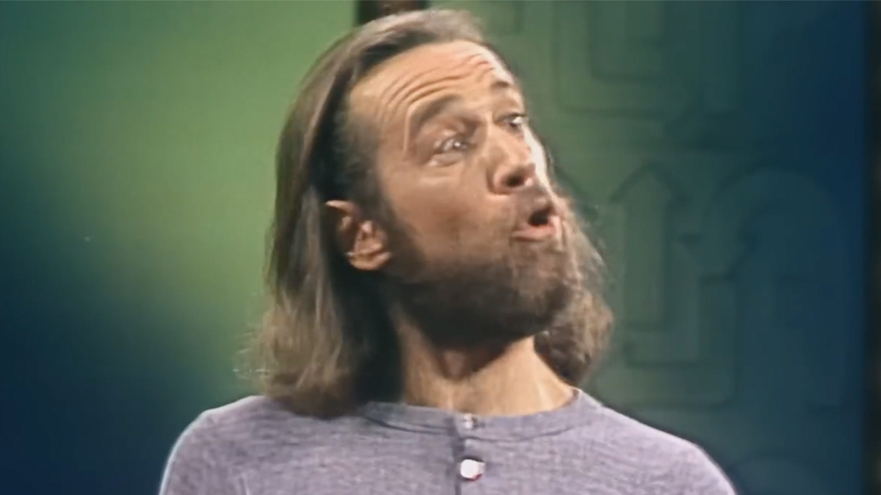 George Carlin, long brown hair and grey shirt, performing standup, footage used in HBO's doc George Carlin's American Dream