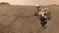 a four-wheeled robot with a head-like box atop a neck-like appendage looks down at a silver tube lying on the dusty reddish-orange surface of Mars