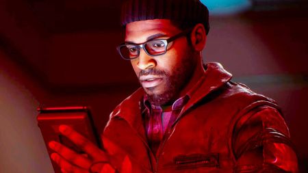 A screencap of the Silent Hill Townfall reveal trailer. A man wearing a beanie and thick glasses peers down at a handheld device. His face is illuminated by the glow of the screen.
