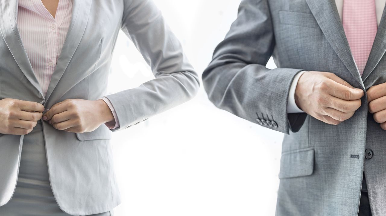 A woman and man stand side by side and button blazers