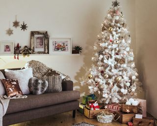 a small apartment with a grey couch and christmas tree in the corner