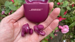 Bose QuietComfort Ultra Earbuds (2nd Gen) in purple color, next to some flowers of a similar shade but held in a hand