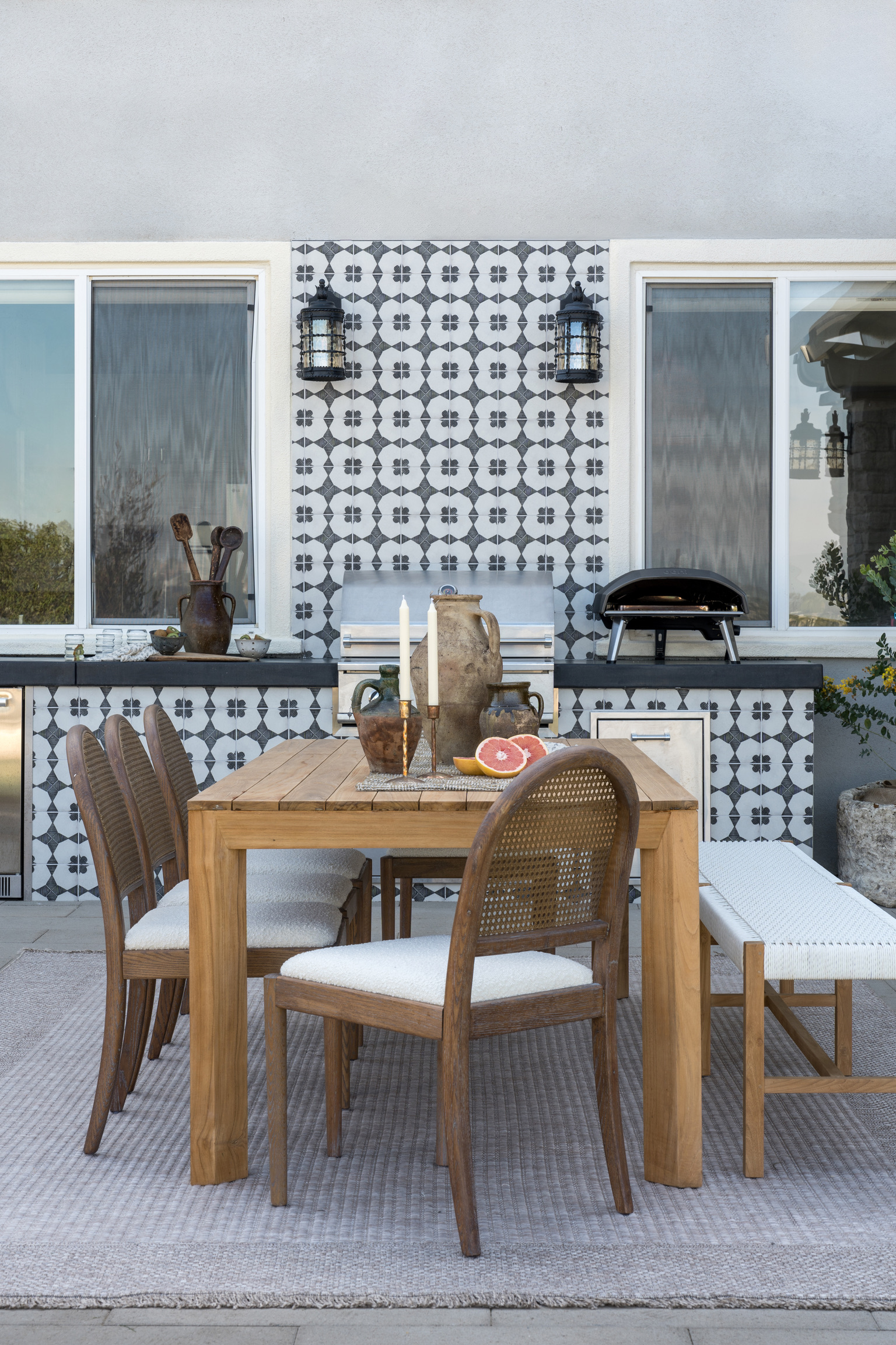 An outdoor kitchen with tiles along the island, backsplash, and a dining table set in front of it