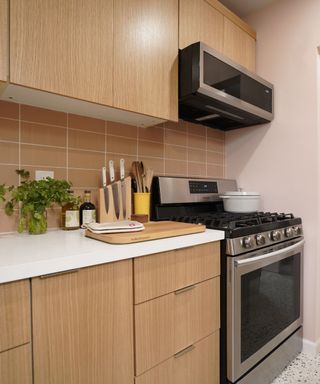 A kitchen with light pink walls, light pink tile backsplash, a stove and set of knives