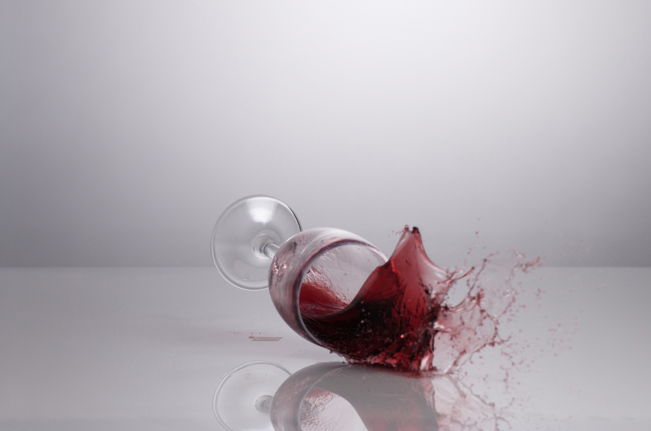 Glass of red wine spilling onto floor
