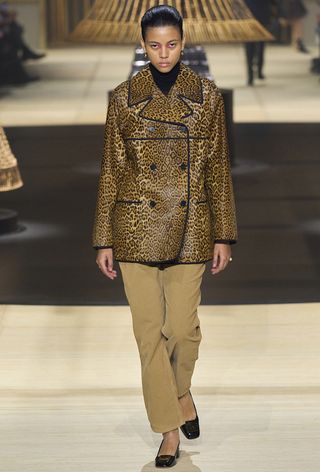 leopard print coat trend is shown on the fall runway 2024 collection of Dior with a model walking wearing a leopard print peacoat over a black sweater with tan trousers and black ballet flats