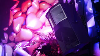 A Funktion-One loudspeaker on a wall with neon pink hearts and purple blue spots. 