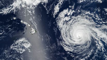 A satellite photo of a swirling hurricane next to a silver streak, or sunglint, that partially obscured the islands of Hawaii
