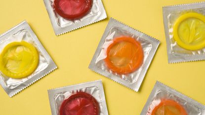red, orange and yellow condoms in wrappers on a solid yellow background