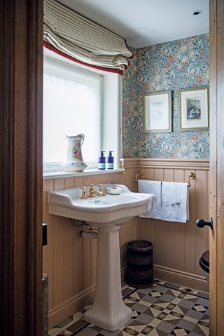 an arts and crafts style bathroom with mismatching wallpaper, floor tiles, and a white sink