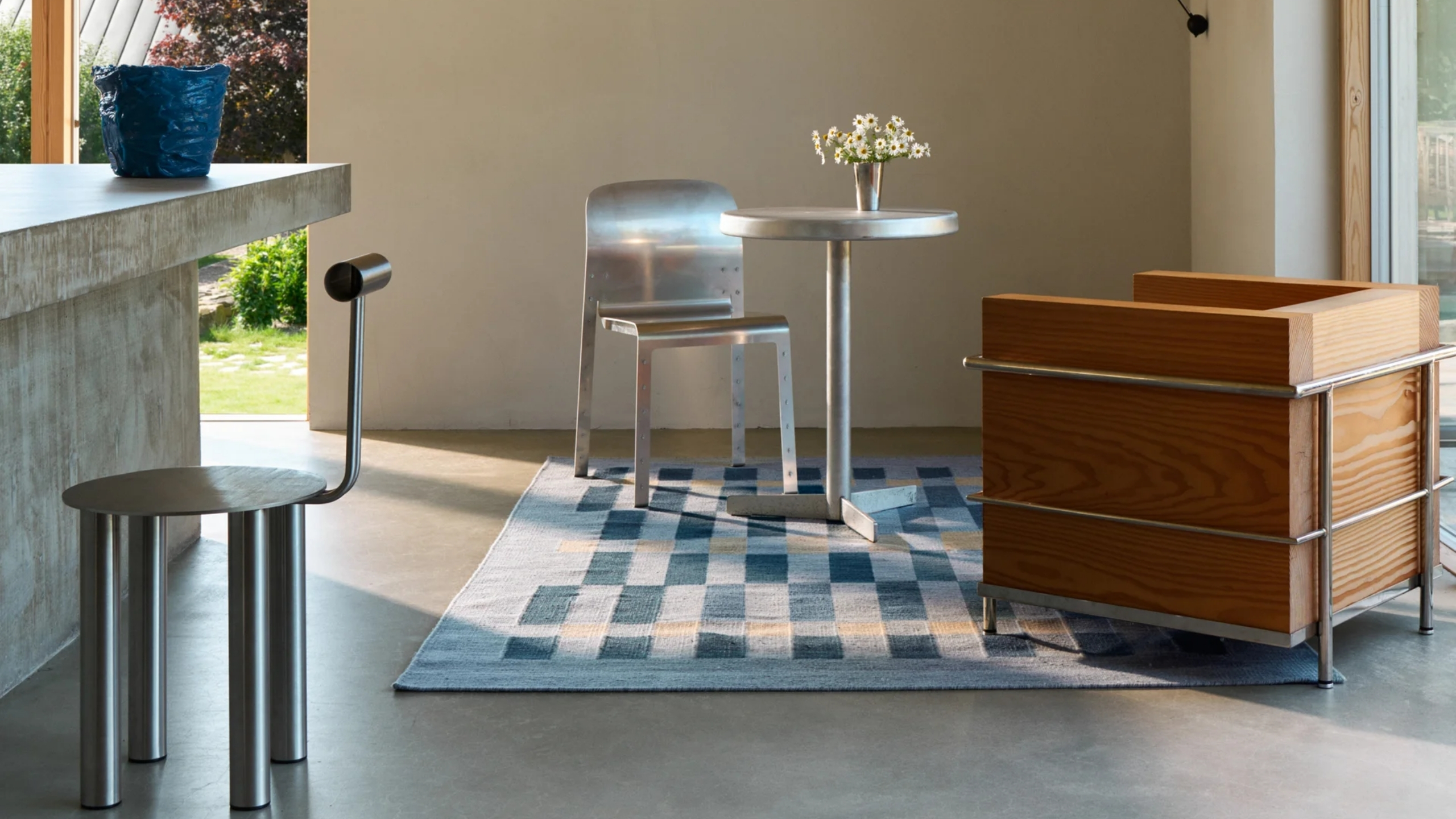 Modern dining area with a blue and cream checked rug, sculptural metal chairs, a round pedestal table and warm wood cabinetry.