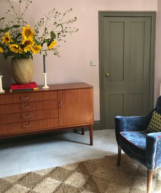 Blush living room with sage green painted door, retro sideboard, sunflowers, coir rug, blue armchair,