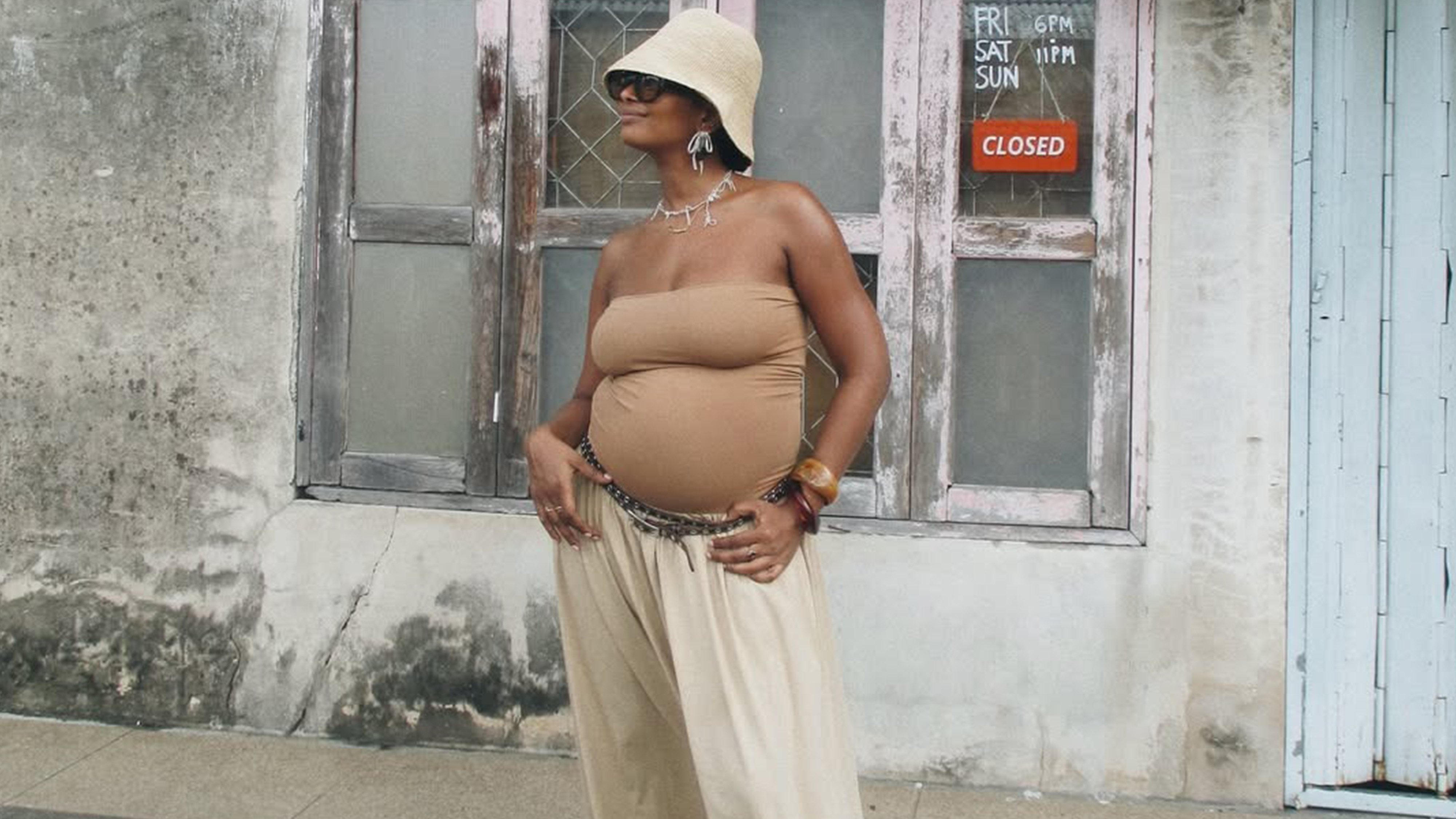A woman wears a hat, beige tube top, and beige pants.