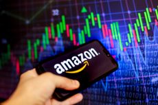 The Amazon logo, an eCommerce online platform, is displayed on a smartphone screen against a stock market chart image