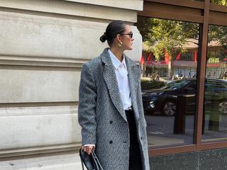 she wears gray coat, white button down black pants with black shoes and black purse