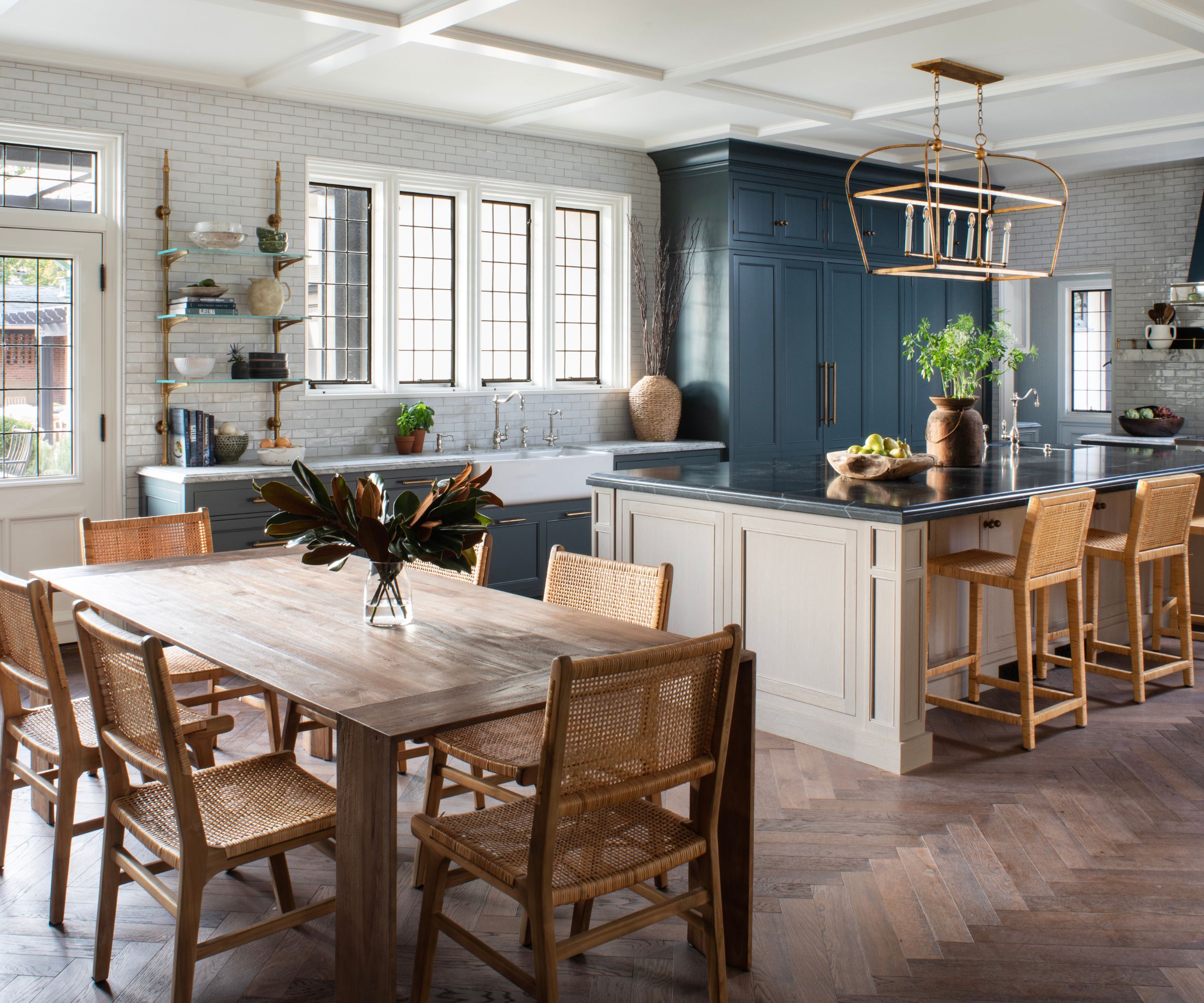 Open plan kitchen with dark gray cabinets and a light beige island with a wooden dining table and rattan seating