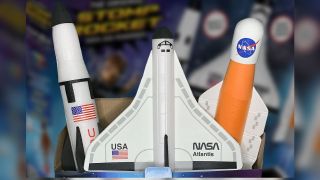 three foam rockets in front of a box with a colorful photo of space on it
