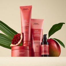 Aveda nurtiplenish pink bottles next to a mango on neutral background