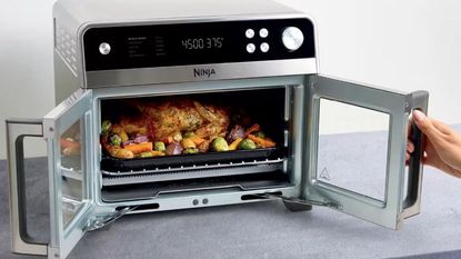 A double door air fryer convection oven unit with glass front doors, and a stainless steel frame being opened on a grey kitchen counter
