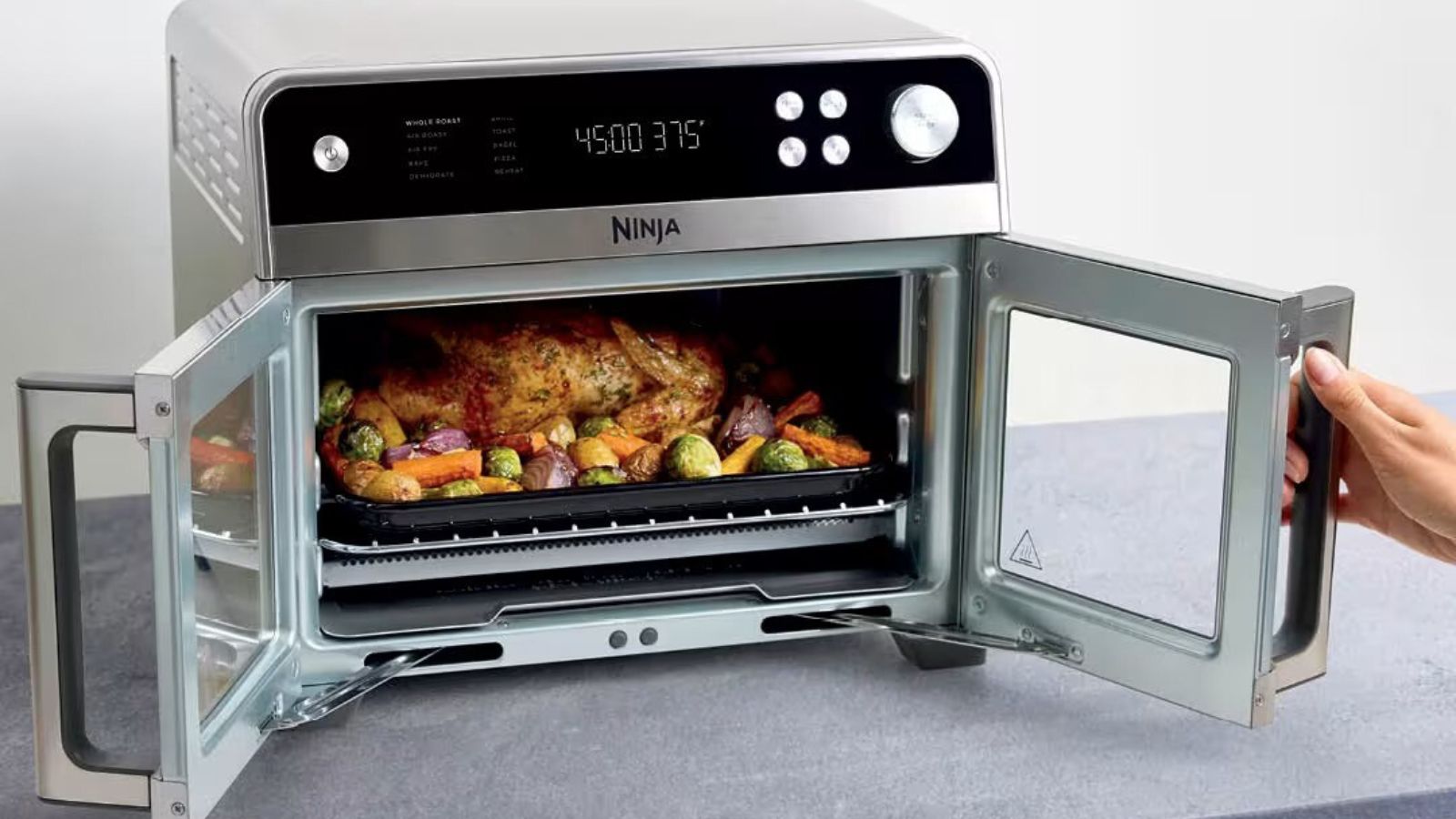 A double door air fryer convection oven unit with glass front doors, and a stainless steel frame being opened on a grey kitchen counter