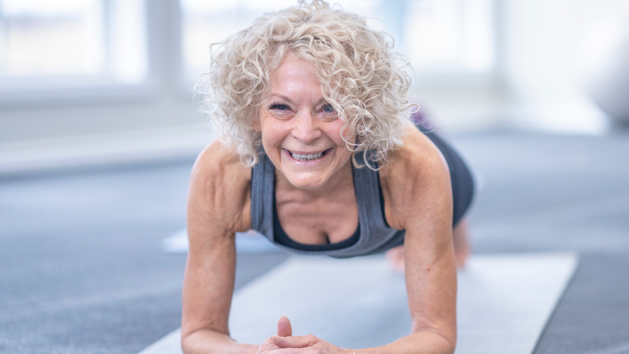 A smiling woman performs a plank exercise on a mat.