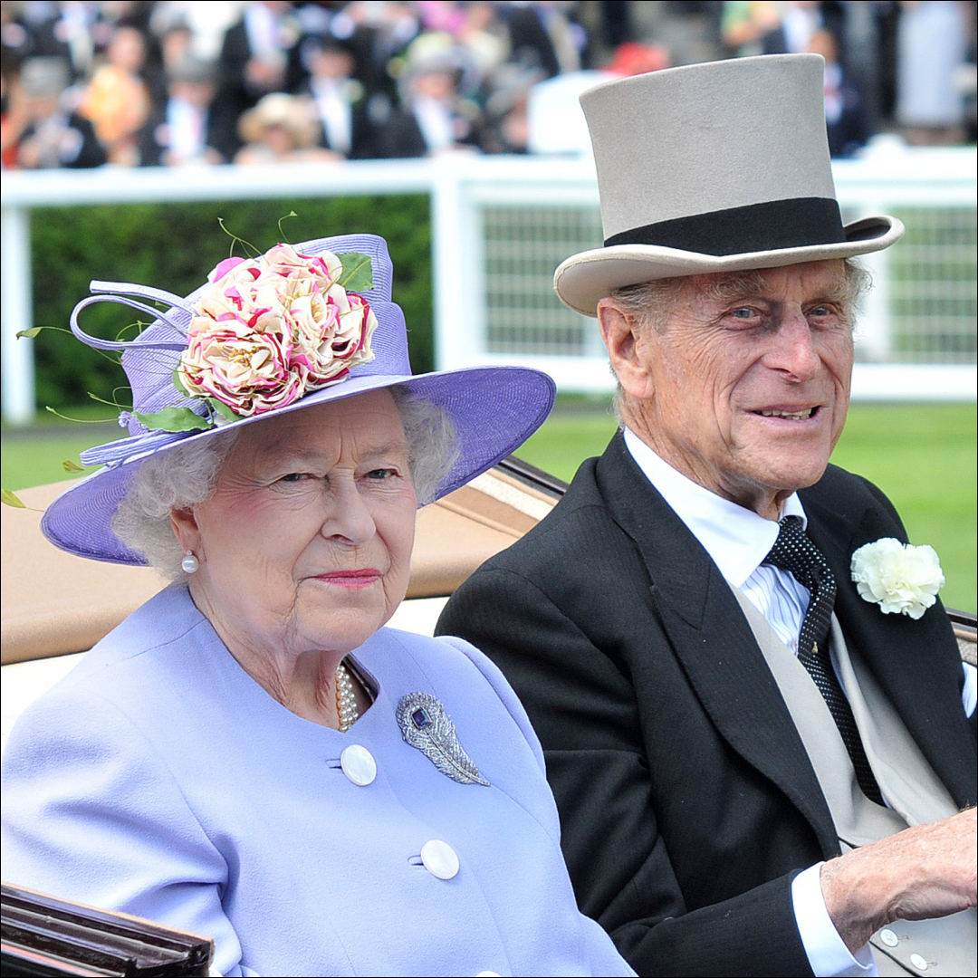 Queen Elizabeth wearing a lilac hat and coat and sitting next to Prince Philip who wears a top hat