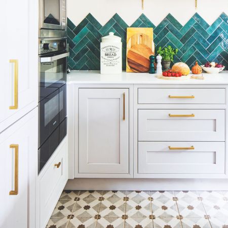 Kitchen with white cabinets and gold handles, with teal tiles on the wall and grey patterned tiles on the floor