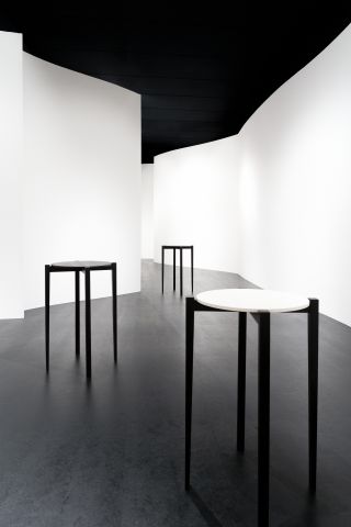 Three small round topped tables in a room with curved white walls and a black floor.