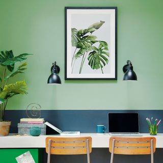 Home office with two toned green walls, two wall lights and botanical print