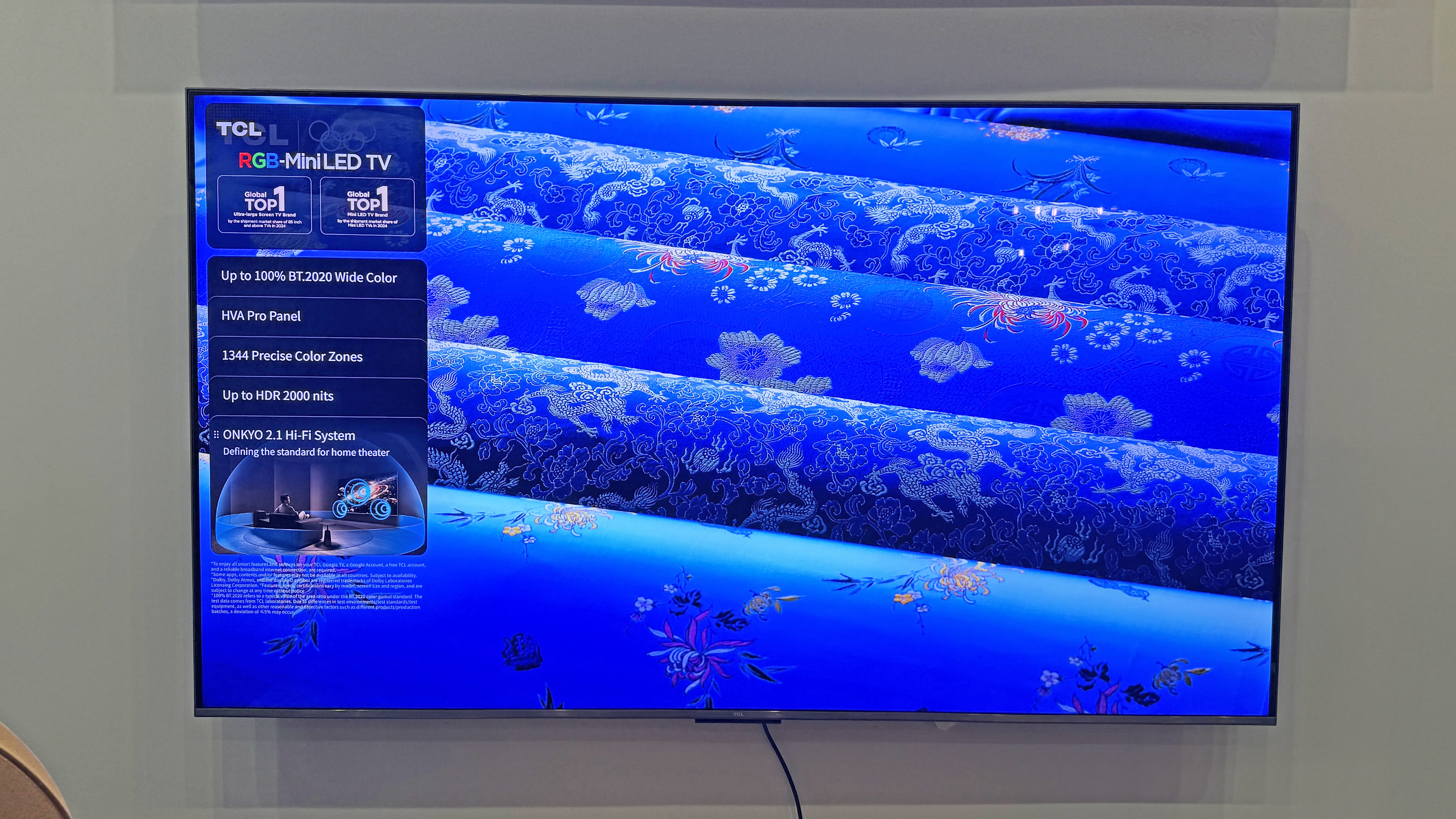 The TCL RM7L TV at a launch event, showing an image of rolls of blue fabric, with a bright and electric tone to the blue color