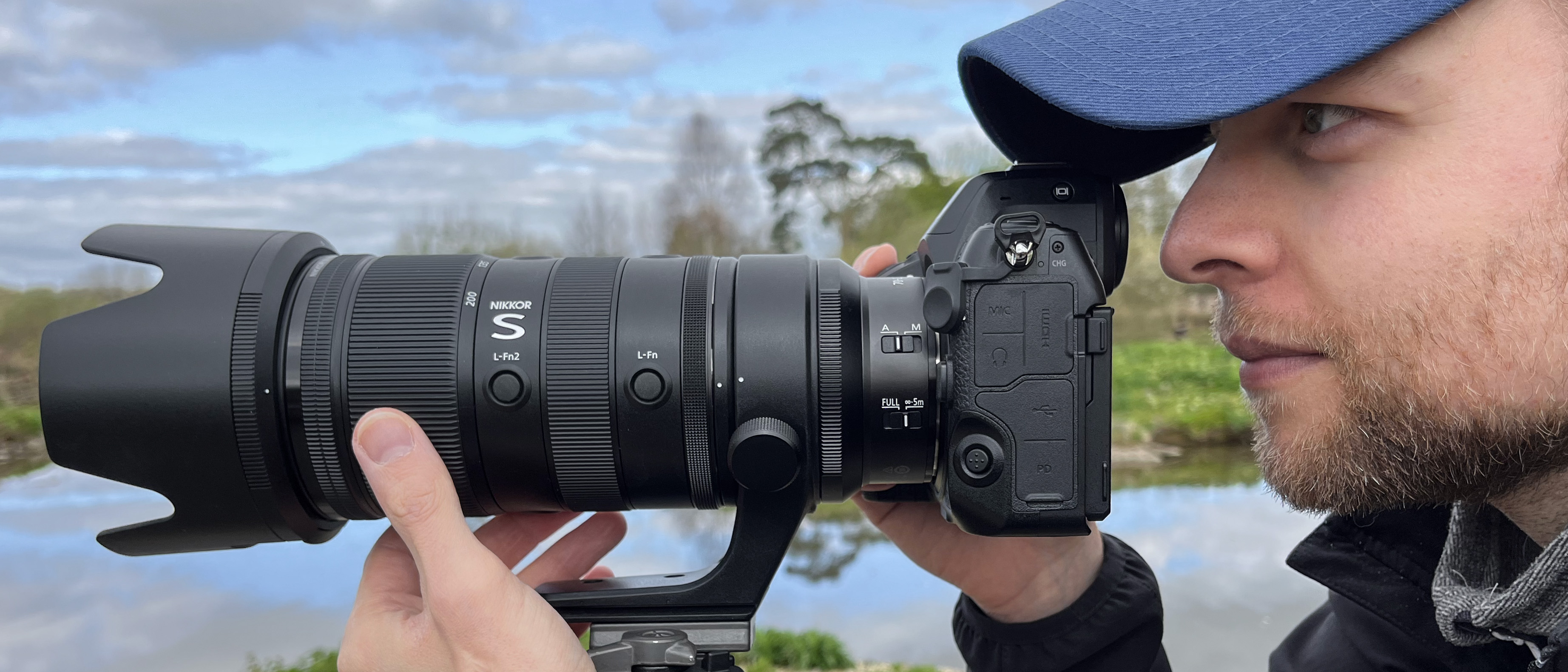 Mike Harris holding Nikon Z 70-200mm f/2.8 VR S II by a lake with vegetation and trees in the background 