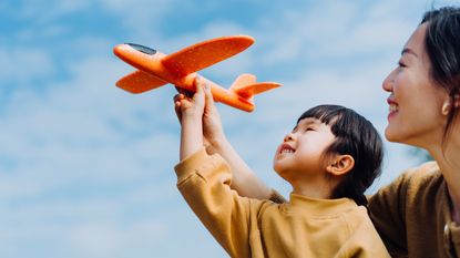 A young girl and her mother together hold up a toy airplane like it's flying through the air.