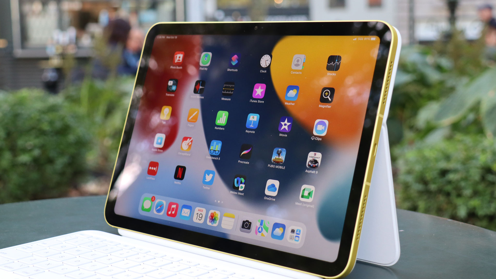 En iPad 10.9 (2022) står på et udendørs bord med startskærmen aktiv, set i en vinkel fra siden.