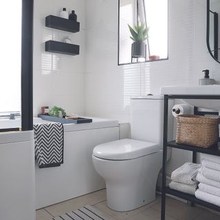 Black and white bathroom with black storage unit and rattan storage baskets.