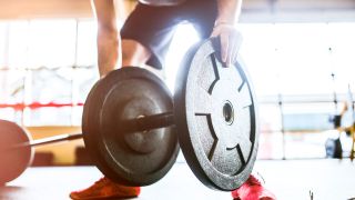 A man loads weight plates onto a barbell before beginning his gym workout routine