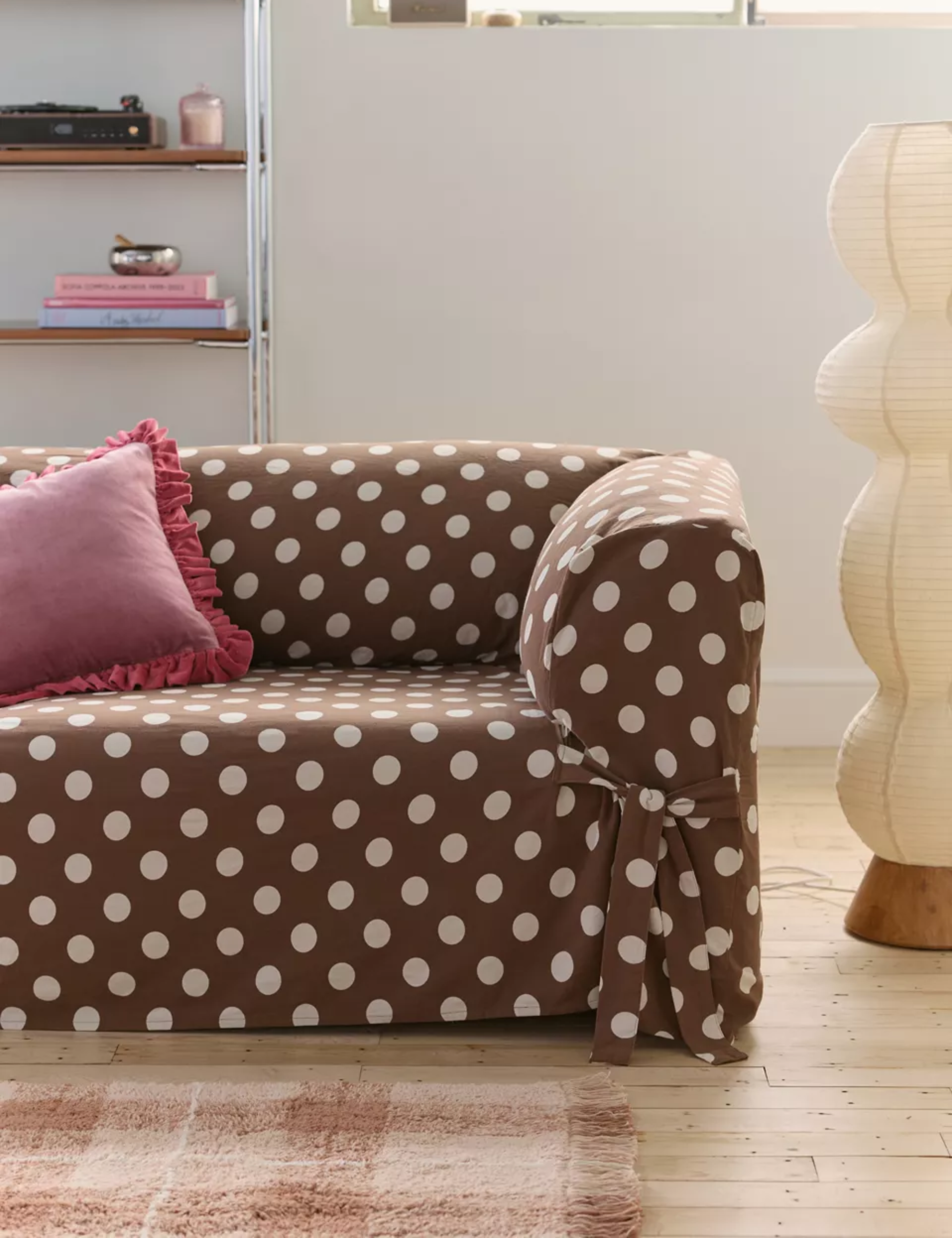 Polka-dot-print slipcovered sofa with a raspberry-pink ruffle-bordered pillow pictured alongside a Noguchi-inspired paper floor lamp
