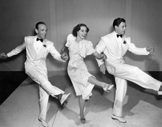 two men in white suits and a woman in a polka dot dress dance in a kickline in Broadway melody