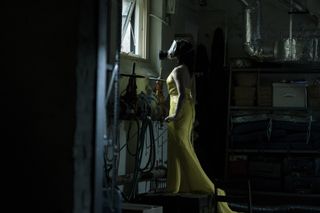 A photo of Sofia Falcone from The Penguin accessorizing a yellow silk halter gown with a gas mask