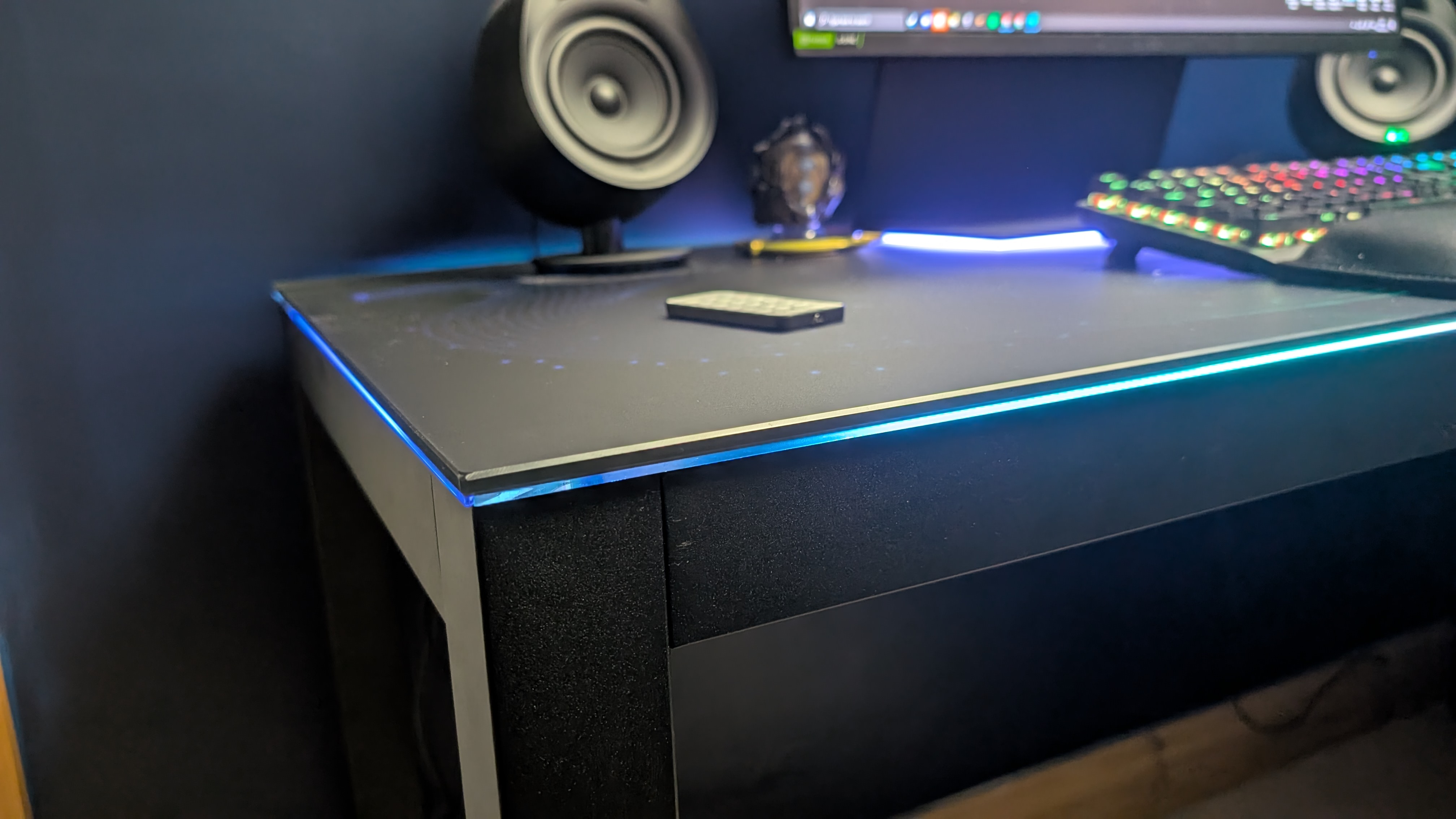 Closeup of one corner of the Eureka Ergonomic GTG Wave gaming desk, showing the RGB lighting that runs around the edges.