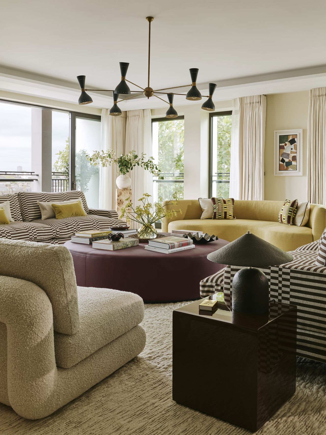 colorful living room with yellow sofa, striped sofas, boucle armchair, oxblood round ottoman coffee table, pendant light, and square side table with lamp