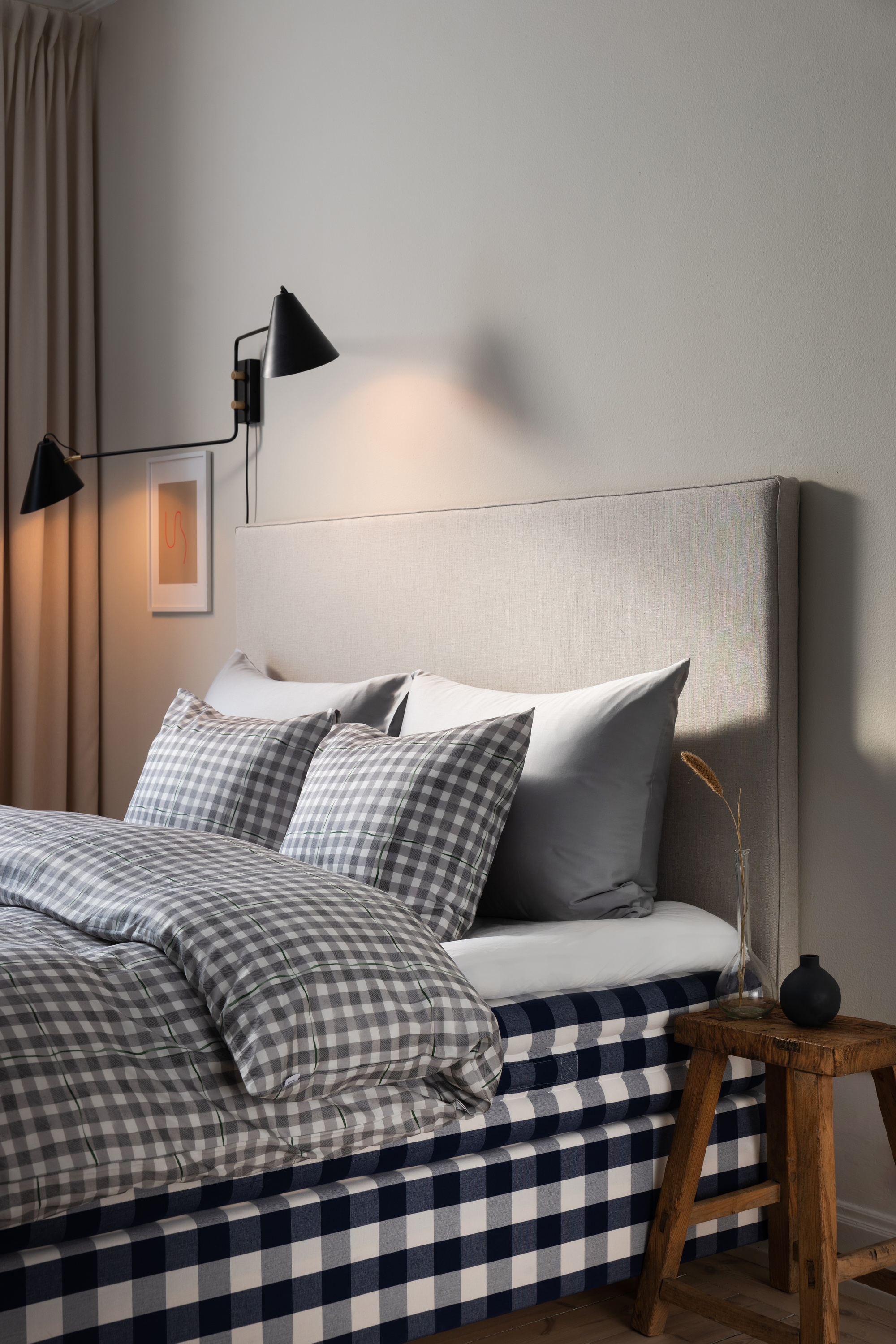 A bedroom with a double bed, a wooden stool as a nightstand, and chequered bedding