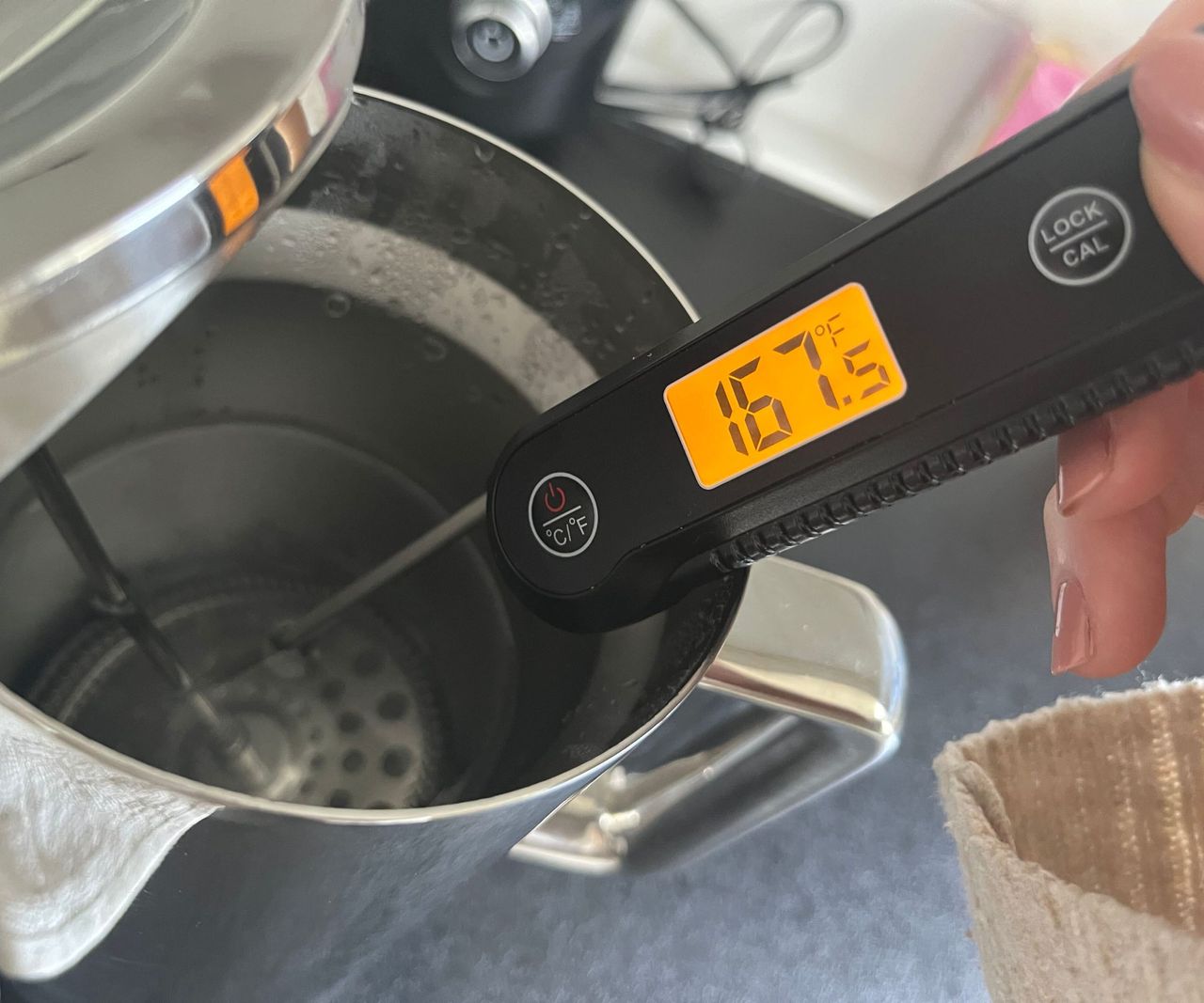a digital thermometer reading the temperature of water in a stainless steel coffee press. It shows 167F