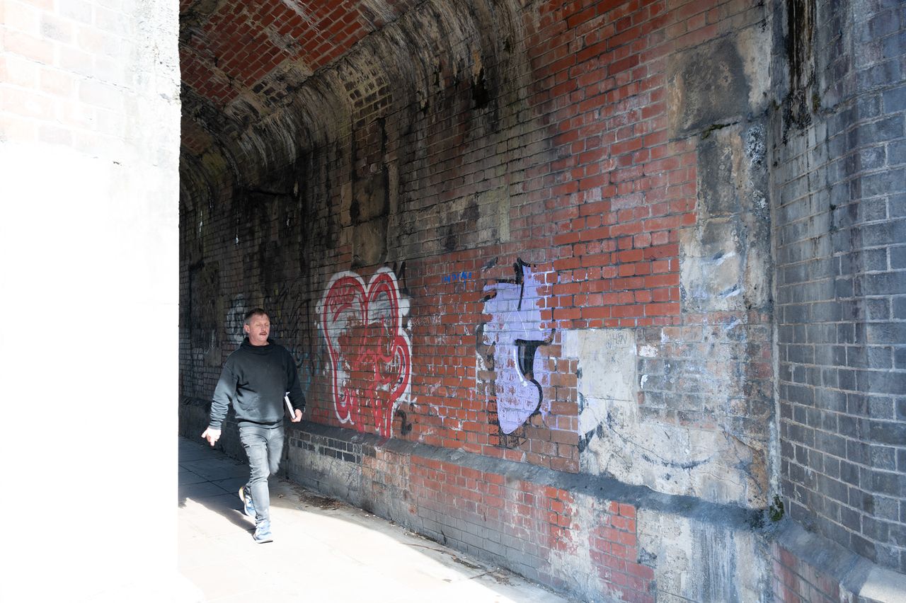 A man walks through a brick underpass with graffiti on the walls