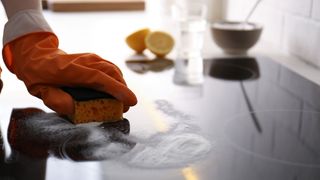 Woman using baking soda to clean electric cooktop indoors