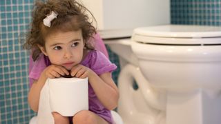 Little girl sitting on toilet.